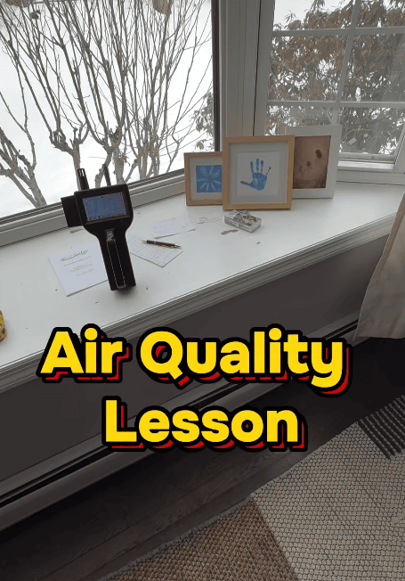 Air quality meter displayed on a windowsill beside framed artwork and notes, with “Air Quality Lesson” text overlay.