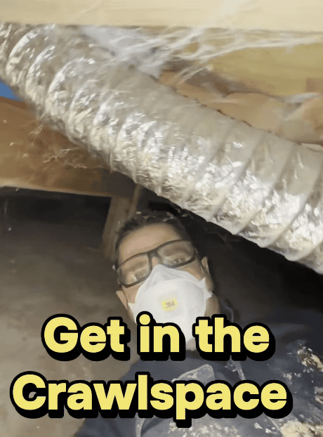 John Skelly wearing protective gear as he climbs through a crawlspace looking for mold.