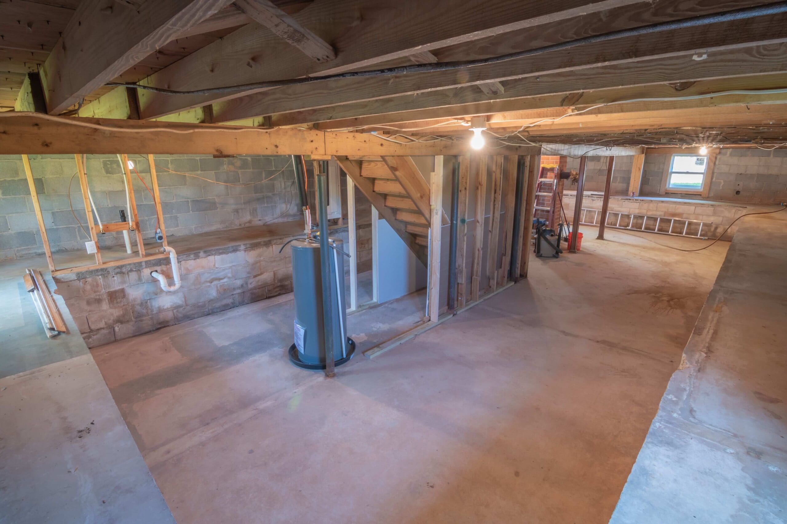 Unfinished basement with exposed wood framing, concrete floors, cinder block walls, plumbing, and a water heater, showing areas that can be evaluated during a mold and moisture inspection.